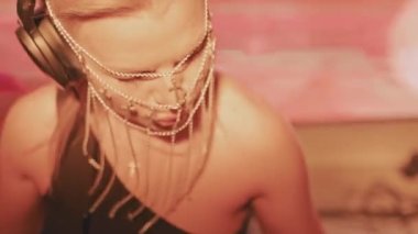 Avrupalı havalı bir bayan DJ, sarı saçlı ve Hıristiyan haçlarından yapılmış şık bir maske, bir gece kulübünde çalışıyor ve dans müziği yaratıyor..