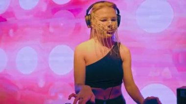 Avrupalı havalı bir bayan DJ, sarı saçlı ve Hıristiyan haçlarından yapılmış şık bir maske, bir gece kulübünde çalışıyor ve dans müziği yaratıyor..