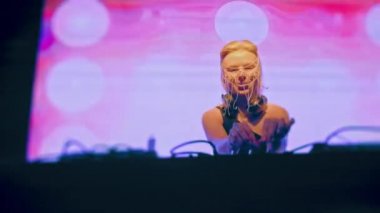 Avrupalı havalı bir bayan DJ, sarı saçlı ve Hıristiyan haçlarından yapılmış şık bir maske, bir gece kulübünde çalışıyor ve dans müziği yaratıyor..