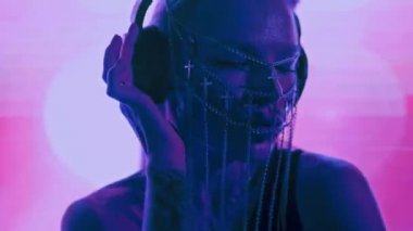 Avrupalı havalı bir bayan DJ, sarı saçlı ve Hıristiyan haçlarından yapılmış şık bir maske, bir gece kulübünde çalışıyor ve dans müziği yaratıyor..