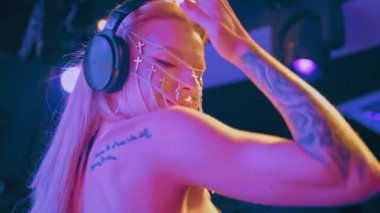 Avrupalı havalı bir bayan DJ, sarı saçlı ve Hıristiyan haçlarından yapılmış şık bir maske, bir gece kulübünde çalışıyor ve dans müziği yaratıyor..