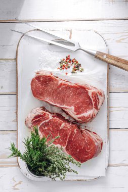 Beyaz ahşap bir tahtada taze çiğ biftek ahşap bir zemin üzerinde tuz ve biberle kırsal bir tarzda..