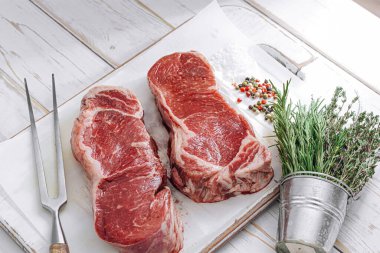 Beyaz ahşap bir tahtada taze çiğ biftek ahşap bir zemin üzerinde tuz ve biberle kırsal bir tarzda..