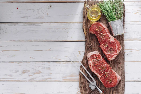 Beyaz ahşap bir tahtada taze çiğ biftek ahşap bir zemin üzerinde tuz ve biberle kırsal bir tarzda..