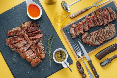 İki biftek striploin ve t-bon, orta pişmiş, sarı arka planda. İki kişilik akşam yemeği.