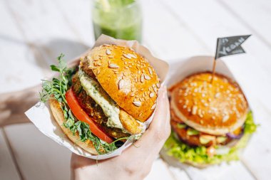 Glütensiz ve keten tohumlu vejetaryen. Nohut burger, roka, turp, avokado salatalığı ve humus. Bitki temelli diyet konsepti. Açık hava kafede oturan bir kadının ellerinde hamburger.