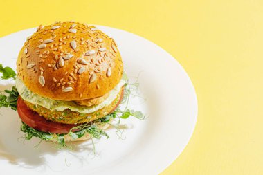 Glütensiz ve etsiz taze vejetaryen burger. Beyaz tabakta sarı arka planda bir burger.
