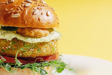 Glütensiz ve etsiz taze vejetaryen burger. Beyaz tabakta sarı arka planda bir burger.