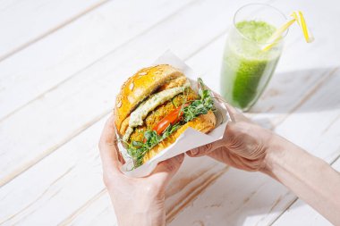 Glütensiz ve etsiz taze vejetaryen burger. Restoranda vejetaryen burger yiyen ve yeşil smoothie içen bir kadın.
