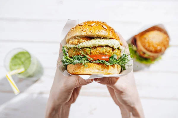 Glütensiz ve keten tohumlu vejetaryen. Nohut burger, roka, turp, avokado salatalığı ve humus. Bitki temelli diyet konsepti. Açık hava kafede oturan bir kadının ellerinde hamburger.