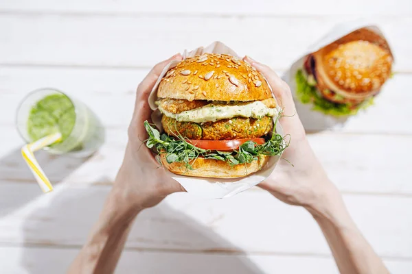 Glütensiz ve keten tohumlu vejetaryen. Nohut burger, roka, turp, avokado salatalığı ve humus. Bitki temelli diyet konsepti. Açık hava kafede oturan bir kadının ellerinde hamburger.