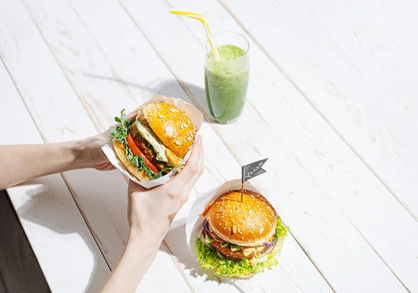 Glütensiz ve etsiz taze vejetaryen burger. Restoranda vejetaryen burger yiyen ve yeşil smoothie içen bir kadın.