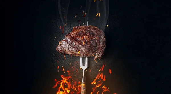 暗い背景に鉄のフォークの上の中珍しいステーキ 下から火と火花を散らし 肉と火 ストック写真