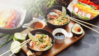 İki kişilik romantik bir yemek. Asya mutfağı, karides, deniz ürünleri, bezelye ve soğanlı pirinç eriştesi. Soya sosu ve çeşitli taze sebzeler. Japon yemek çubuklarıyla siyah tabakta romantik bir akşam yemeği.