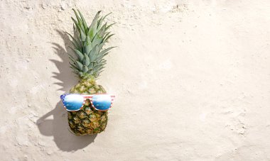 Sahilde ananas, beyaz kumsalda güneş gözlükleriyle Amerikan bayrağı gibi stilize edilmiş.