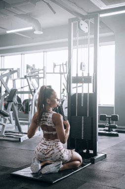 Spor salonunda eşofmanlı genç siyahi kadın spor aletleri üzerinde egzersiz yapıyor.