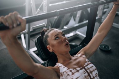 Spor salonunda eşofmanlı genç siyah kadın halteri kaldırıyor.