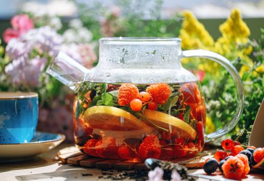 Şeffaf bir çaydanlıkta doğal aromatik meyve çayı ve böğürtlen ve çiçeklerin arasında bir fincanda. Böğürtlen ve kır çiçekleri aromalı sıcak aromatik çay..