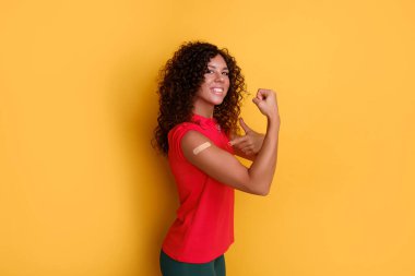 Koyu tenli, mutlu yüzlü, kolunda alçı olan bir kadın. Kovid aşısı olduğu yerde. Aşı olduktan sonra gülümsüyor.