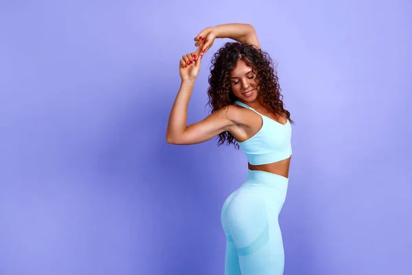 Mutlu, neşeli, anlamlı ve tatmin olmuş siyahi Afro-Amerikan kadınının fotoğrafı. Kadın spor yapıyor, kaslarını esnetiyor.