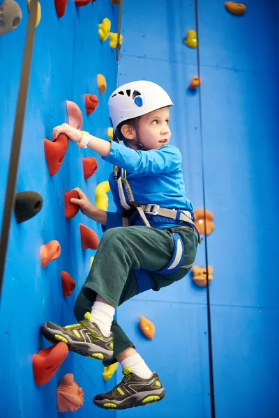 Little boy is climbing in sport park on blue wall — 스톡 사진