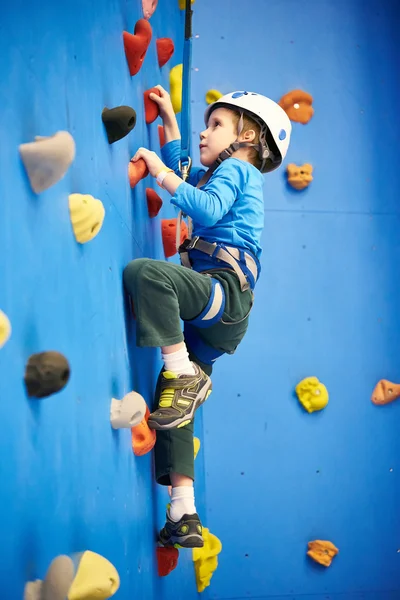 Little boy is climbing on blue wall — 图库照片