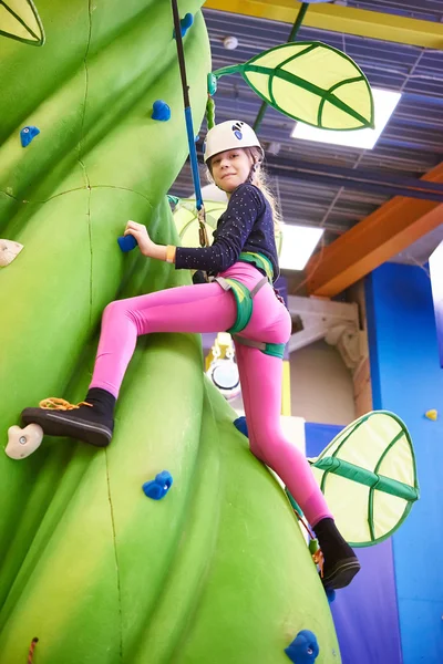 Girl athlete climbing on artifical green tree — Stock fotografie