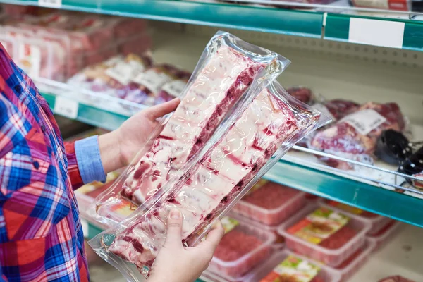 Mulher escolhe costelas de porco na loja — Fotografia de Stock