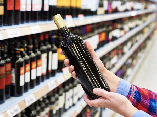 Woman with bottle of red wine in store — Stock Photo, Image