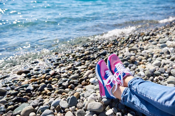 Sneakers flicka på bakgrund av havet och stenig strand — Stockfoto