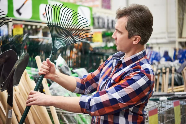 Man chooses rake leaves in store for garden — Stock Photo, Image