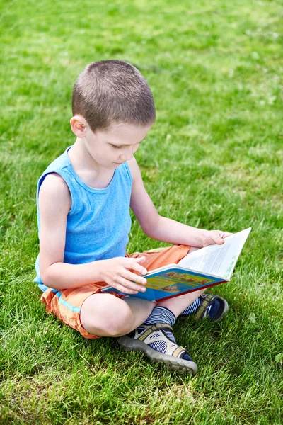 Kleiner Junge liest Buch outdoori auf Gras — Stockfoto