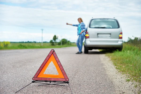 Чрезвычайный знак и женщина ждет помощь рядом с ее машиной — стоковое фото