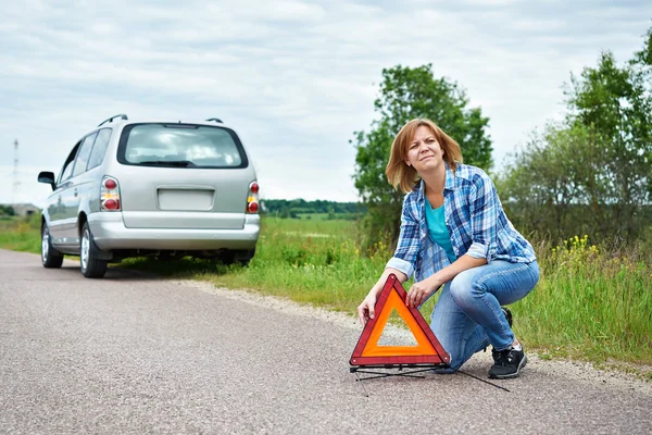 Žena, instalace nouzové znamení na silnici poblíž auto — Stock fotografie