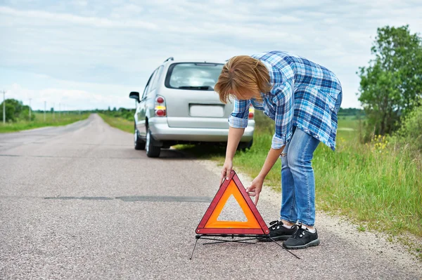 Kvinnan installera akuta tecken på vägen nära bil — Stockfoto