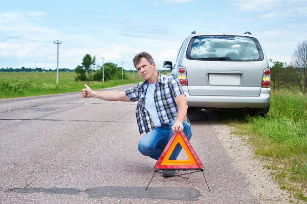 Man op weg in de buurt van noodsituaties teken en weergegeven: duimschroef opwaarts — Stockfoto