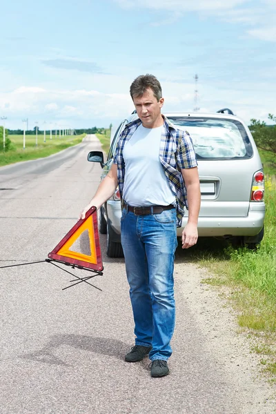 Hombre instalando señal de emergencia en la carretera cerca de su coche — Foto de Stock