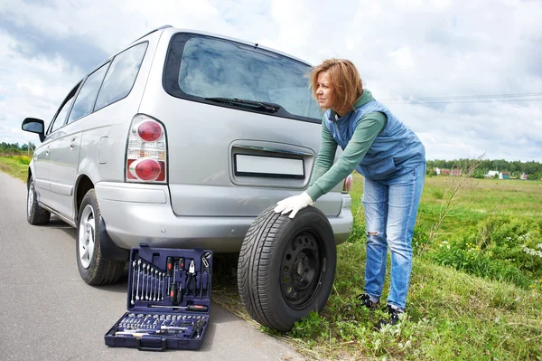 Mujer cambiando una rueda de coche en la carretera — Foto de Stock