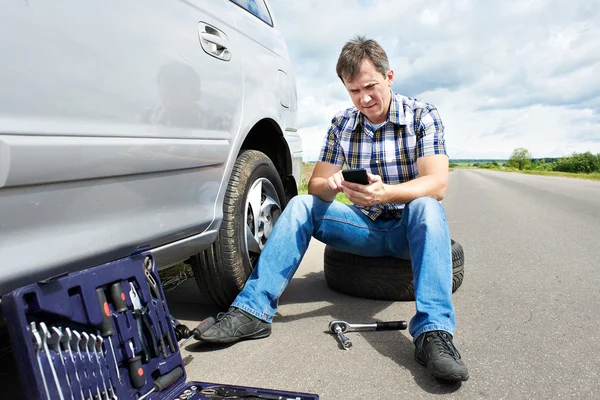 Man met telefoon eist in dienst van reservewiel auto — Stockfoto