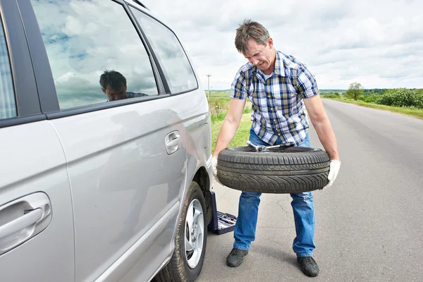 El hombre cambiando un neumático de repuesto del coche Imagen de archivo