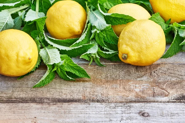 Lemons with leaves of mint on wooden table — Stock Photo, Image