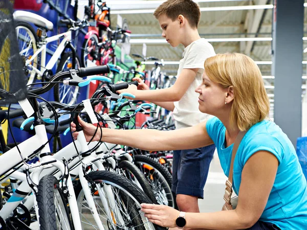 男の子とお母さんはスポーツ用品店で自転車を選ぶ — ストック写真