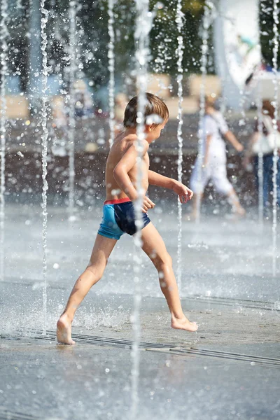 Niño corriendo a través de las fuentes en el clima caliente — Foto de Stock