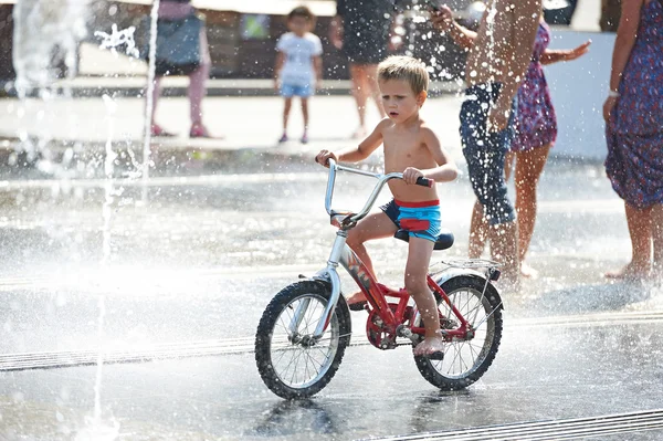 Little boy rides his bike among fountains — Stock Photo, Image