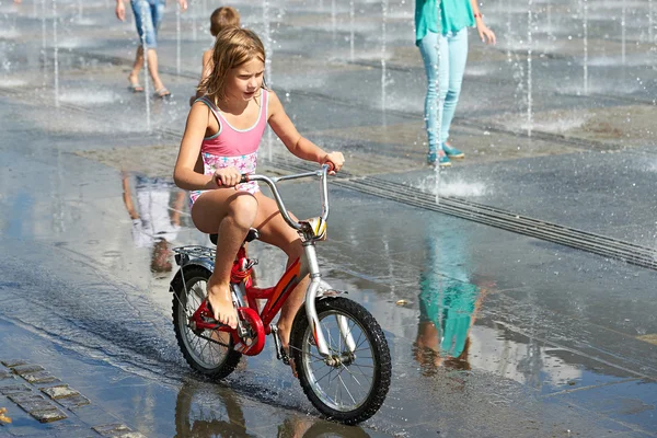 Petite fille monte son vélo parmi les fontaines — Photo