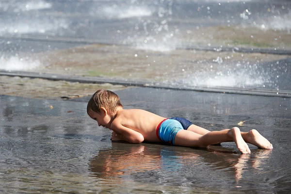 Kleine jongen liggend in een plas — Stockfoto