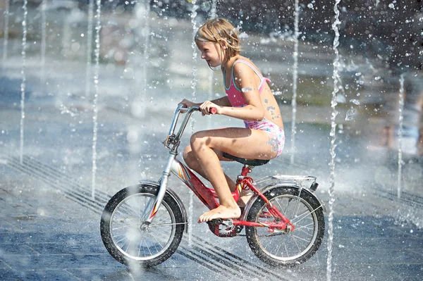 Little girl rides his bike among fountains — Stock Photo, Image