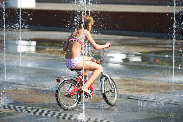 Liten flicka rider sin cykel bland fontäner — Stockfoto