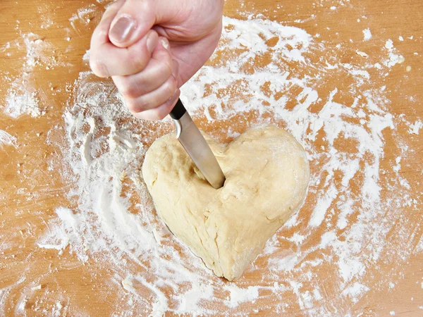 Hand with knife struck heart of dough — Stock Photo, Image