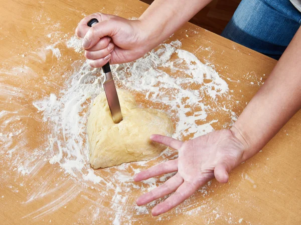 Nervous woman pierces heart of dough with kitchen knife — Stock Photo, Image